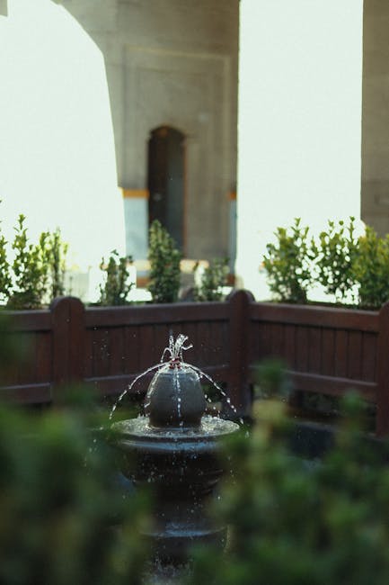 A cozy garden scene featuring a wooden bench with a decorative backrest placed on a curved brick pathway, surrounded by a variety of lush green plants and ornamental grasses. Dense foliage, including 